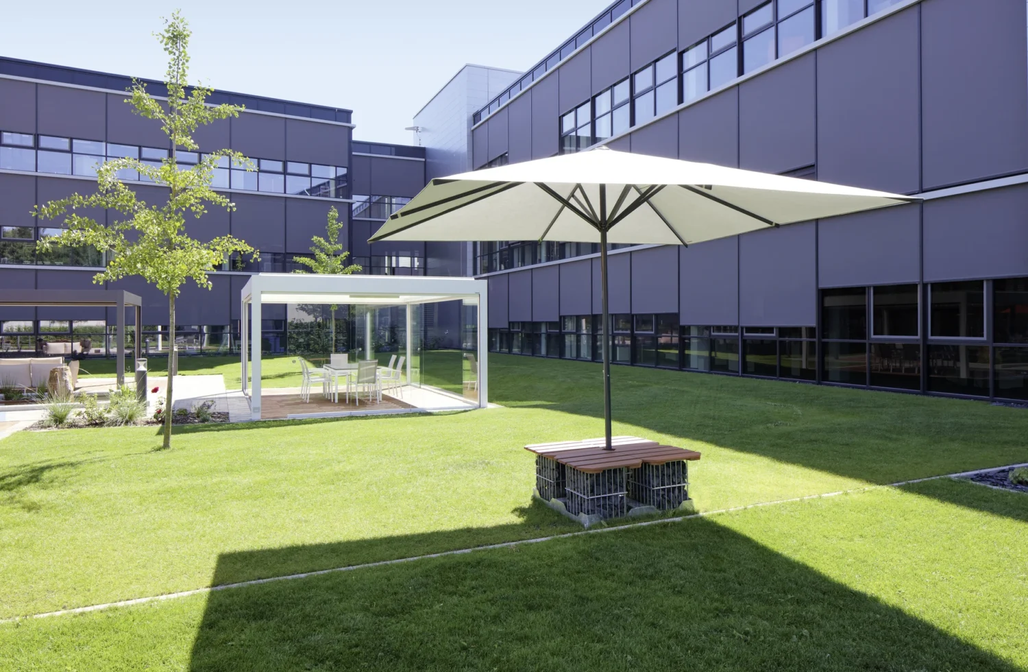 Moderne Außenansicht eines Bürogebäudes mit Sonnenschirm und Grünfläche