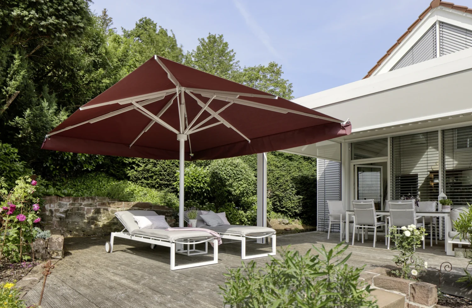 Großer roter Sonnenschirm auf einer Terrasse mit Sonnenliegen und Gartenmöbeln